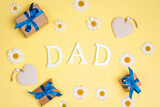 Word Dad with chamomile flowers, gifts and hearts on yellow background.