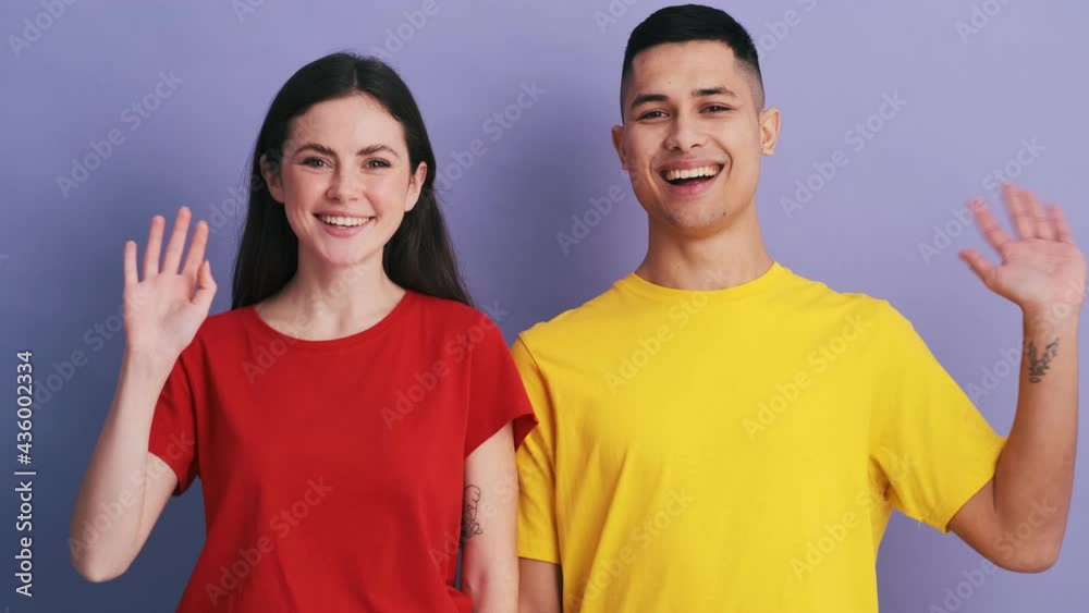 The smiling couple waving at the camera while standing in the purple studio The smiling couple waving at the camera while standing in the purple studio