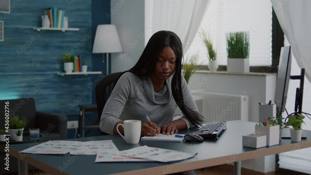 Black student drinking coffee while searching business information on internet using computer working at communication project. Focused woman sitting at desk in living room analyzing homework graphic Black student drinking coffee while searching business information on internet using computer working at communication project. Focused woman sitting at desk in living room analyzing homework graphic