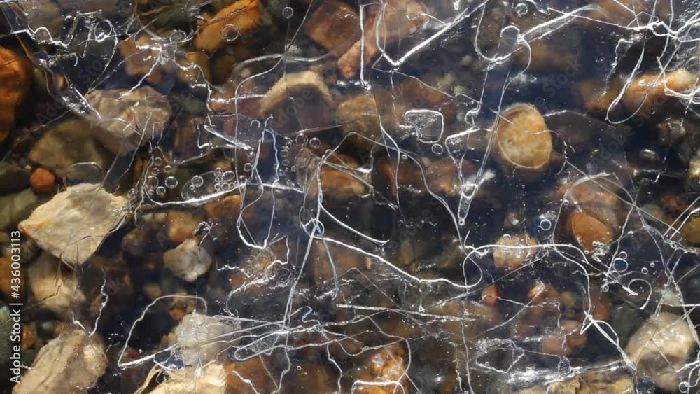 Several layers of ice cover the shingle bottom of the river. The swaying water moves the air bubbles rhythmically. Abstract moving picture. Several layers of ice cover the shingle bottom of the river. The swaying water moves the air bubbles rhythmically. Abstract moving picture.