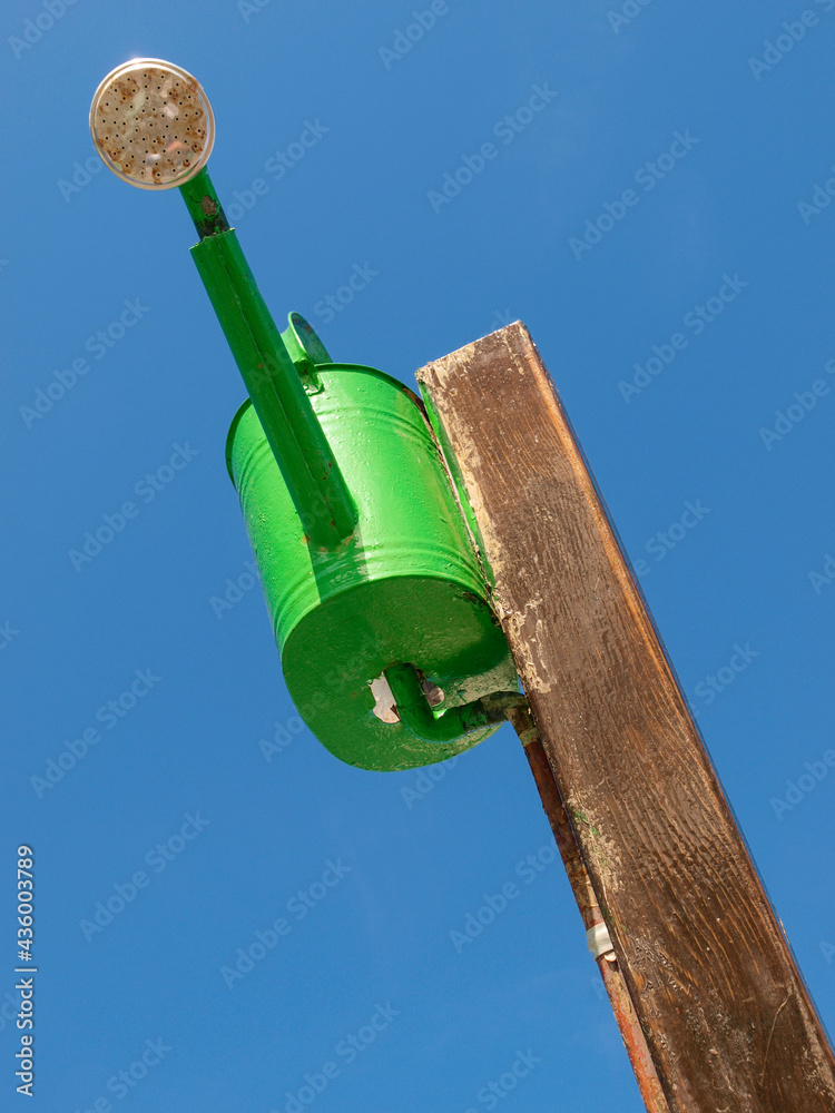 Fototapeta premium Regadera de metal verde colgada de un poste de madera a modo de ducha