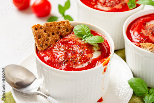 Tomato soup with crispbread and basil in white bowls on a gray background. Tasty summer food.