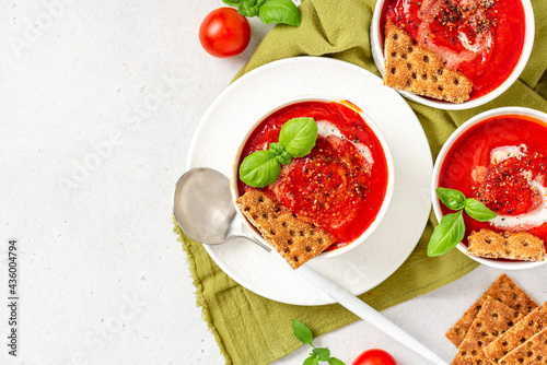 Fototapeta Naklejka Na Ścianę i Meble -  Tomato soup with crispbread and basil in white bowls on a gray background top view. Tasty summer food. Copy space for text.