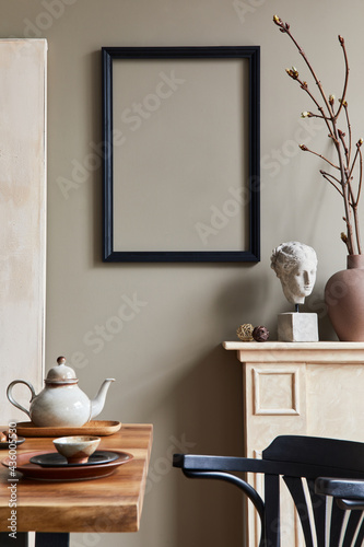 Rustic interior design of dining room with wooden family table, candelstick, retro chair, cup of coffee, decoration, mock up picture frame and elegant personal accessories. Beige wall. Template. © FollowTheFlow