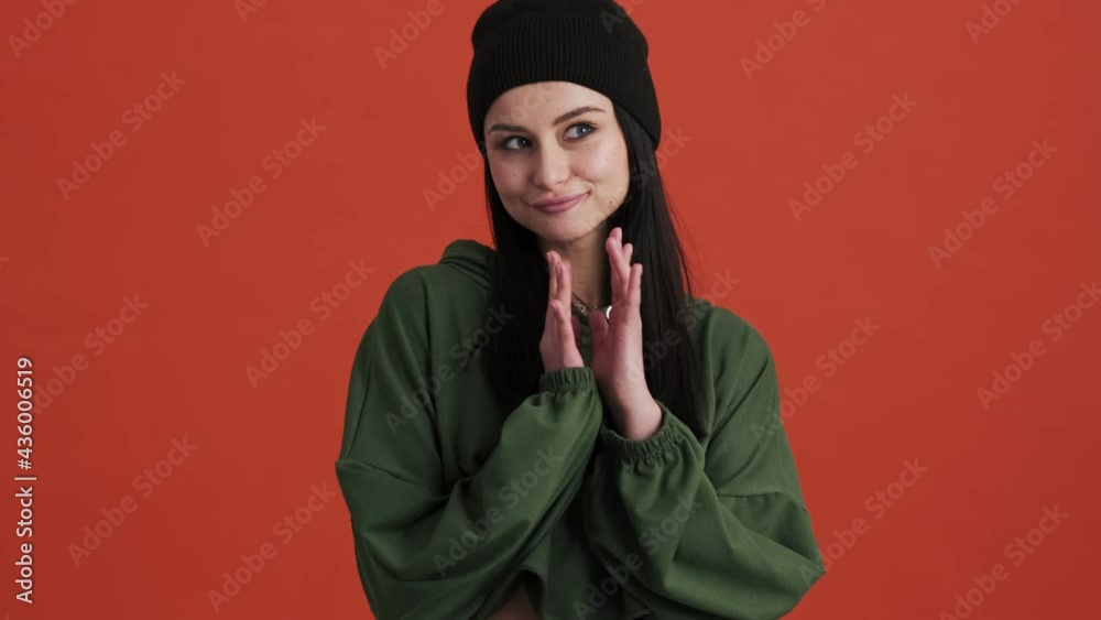 A pleased woman wearing hoodie is thinking about something standing isolated over red wall in the studio A pleased woman wearing hoodie is thinking about something standing isolated over red wall in the studio