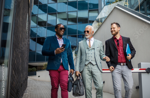 Three business men walking and talking outside. Man holding mobile