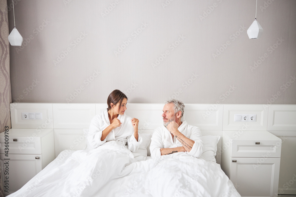 Angry married couple in white bathrobes looking to each other while gesturing in home apartment Angry married couple in white bathrobes looking to each other while gesturing in home apartment