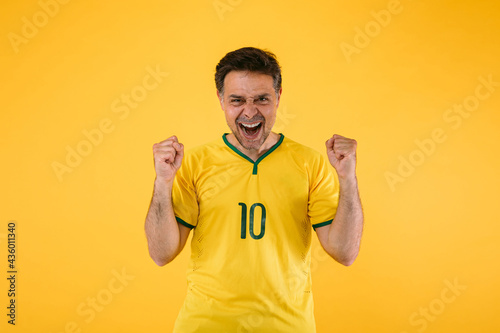 Brazilian soccer fan in a yellow jersey clenches his fists and yells cheering for his team.
