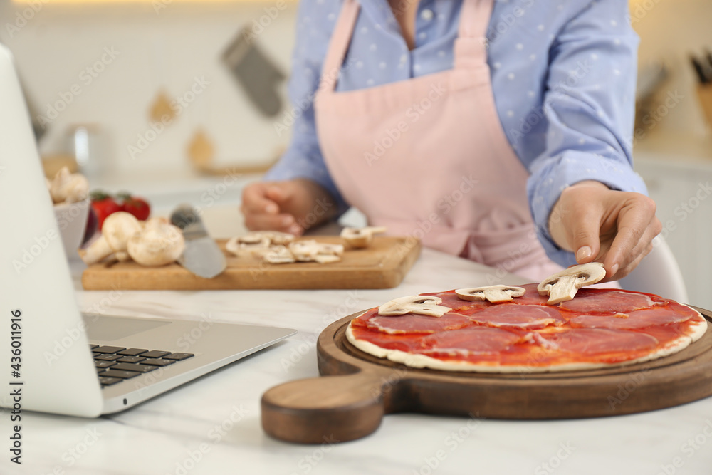 Woman making pizza while watching online cooking course via laptop in kitchen, closeup