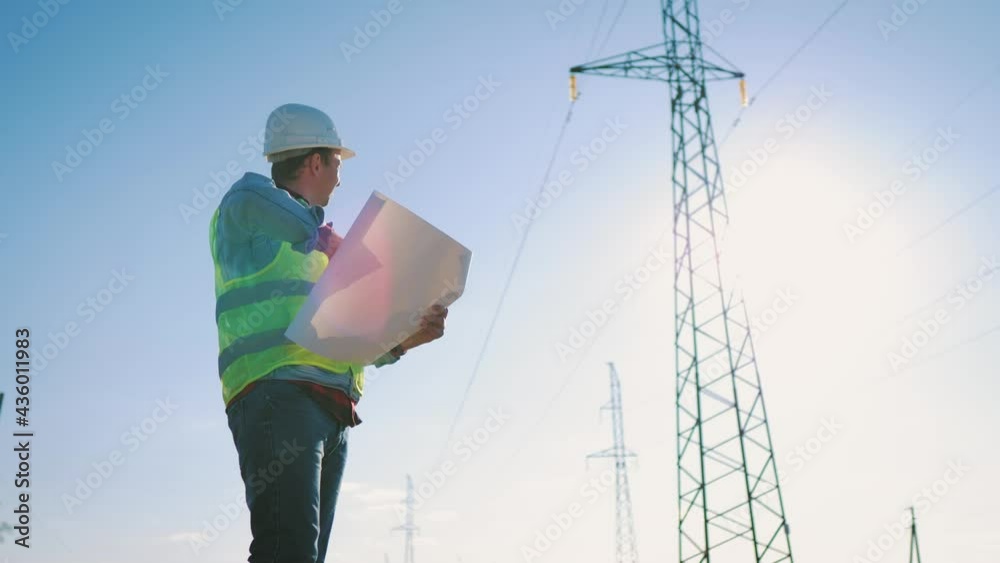 Electricity Work Concept. Silhouette Of Engineer In Helmet Standing On Field With Electricity Towers. Electrical Engineer With High Voltage Electricity Pylon At Sunset. Voltage Tower Support. Electricity Work Concept. Silhouette Of Engineer In Helmet Standing On Field With Electricity Towers. Electrical Engineer With High Voltage Electricity Pylon At Sunset. Voltage Tower Support.