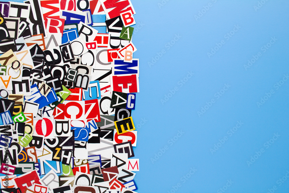 Obraz premium Alphabet letters cutting from paper magazine on blue background with copy space for text. Abstract collage from clippings with newspaper magazine letters.