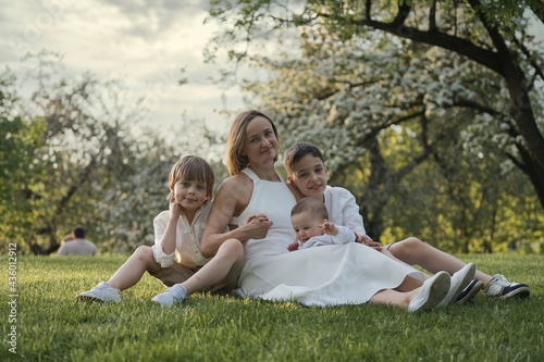 Mother and three children hugging. Happy family sitting outdoor: woman and two brother kids boys and cute little toddler boy