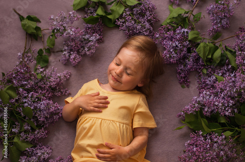 a child in yellow clothes sleeps with a smile on his face  and beautiful flowers are laid out around him