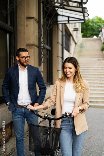 Young businesswoman standing on the street with bicycle. Beautiful businesswoman talking with her colleague