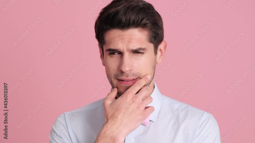 A serious young man wearing a bow tie is thinking about something standing isolated over a pink wall in the studio A serious young man wearing a bow tie is thinking about something standing isolated over a pink wall in the studio