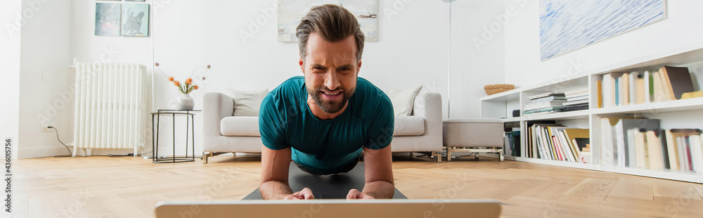frowning man training in plank pose near laptop, banner frowning man training in plank pose near laptop, banner