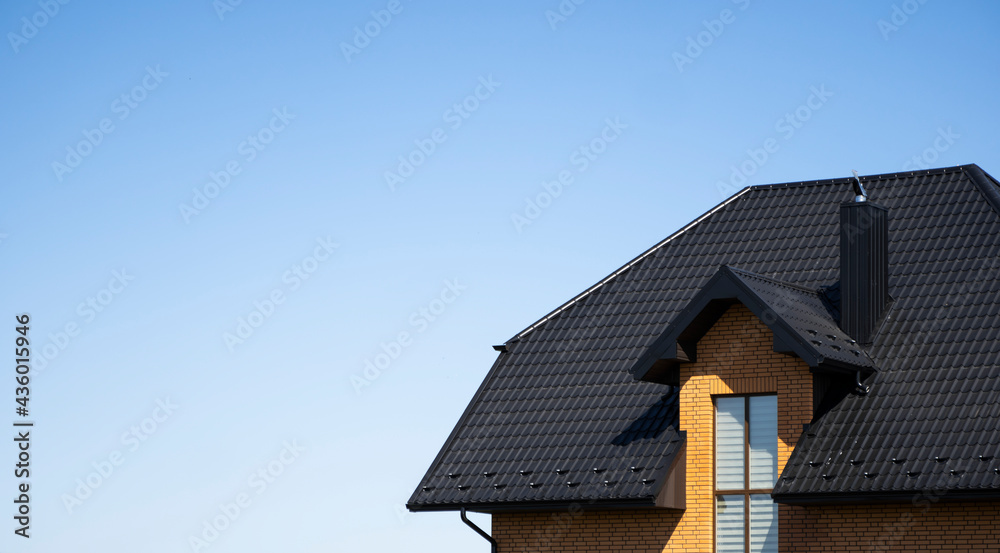 Brown corrugated metal profile roof installed on a modern house with a attic windows. The roof of corrugated sheet. Roofing of metal profile wavy shape. Modern roof made of metal. Metal roofing. Brown corrugated metal profile roof installed on a modern house with a attic windows. The roof of corrugated sheet. Roofing of metal profile wavy shape. Modern roof made of metal. Metal roofing.