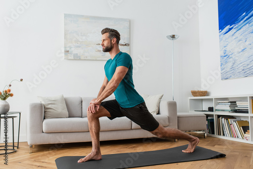 sportive man practicing crescent lunge pose on yoga mat at home photo