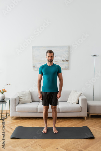 sportive barefoot man looking at camera while standing in mountain pose at home