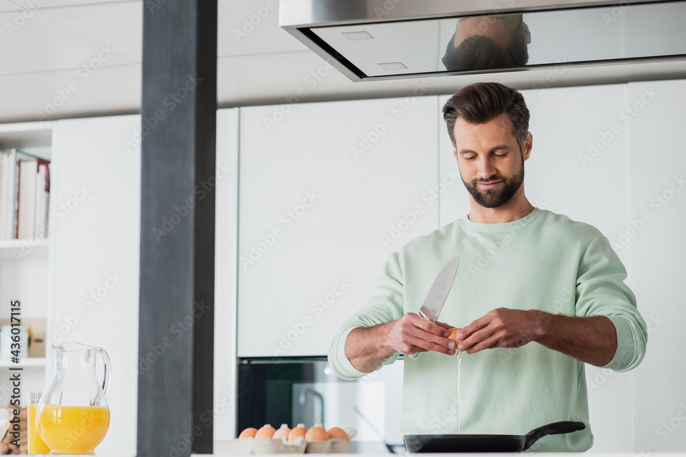 positive man braking chicken egg near frying pen while preparing breakfast positive man braking chicken egg near frying pen while preparing breakfast
