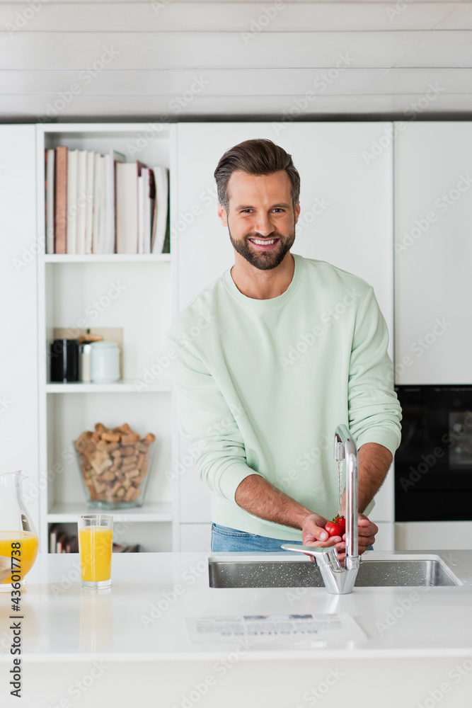 man smiling at camera while washing cherry tomatoes in kitchen man smiling at camera while washing cherry tomatoes in kitchen