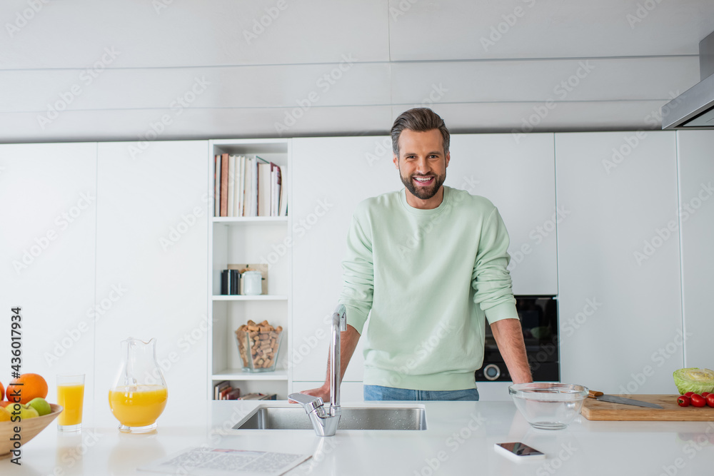 cheerful man smiling at camera near orange juice and sink in kitchen cheerful man smiling at camera near orange juice and sink in kitchen