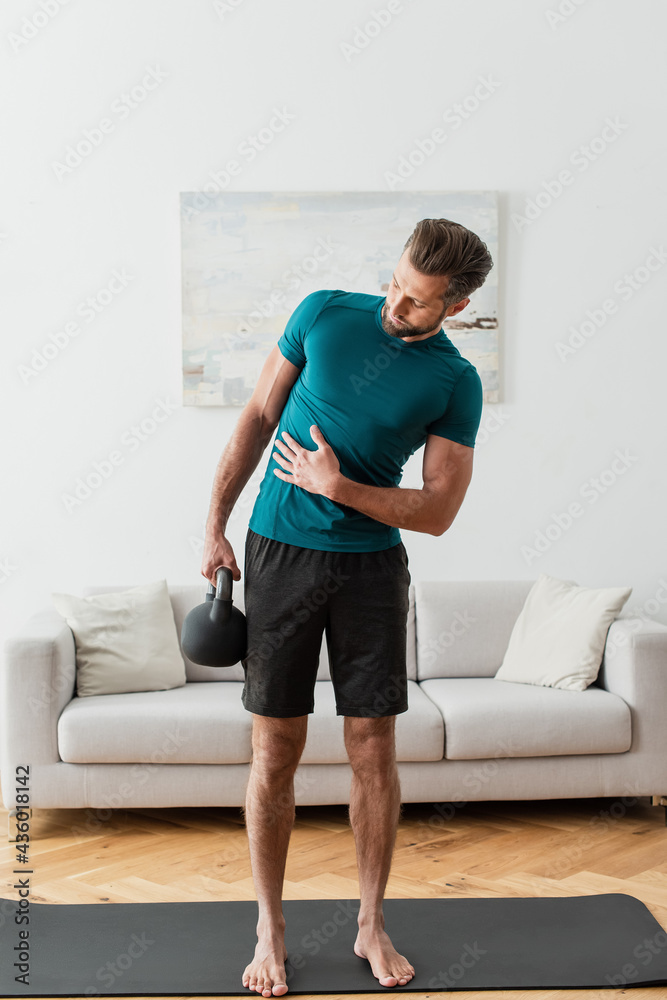 full length view of barefoot man lifting kettlebell in living room full length view of barefoot man lifting kettlebell in living room