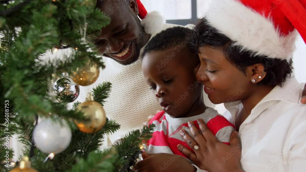 family, winter holidays and people concept - happy african american mother, father and baby son decorating christmas tree at home on family, winter holidays and people concept - happy african american mother, father and baby son decorating christmas tree at home on
