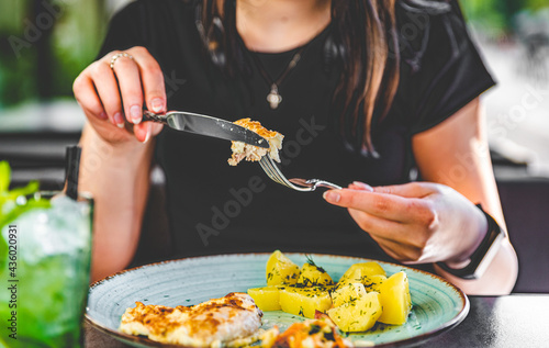 woman hand holding fork and knife eat chicken breast meat with potato in a plate