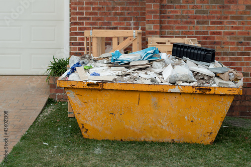 Skip bin full of household waste rubbish on the front yard. House clean up and renovation concept. photo