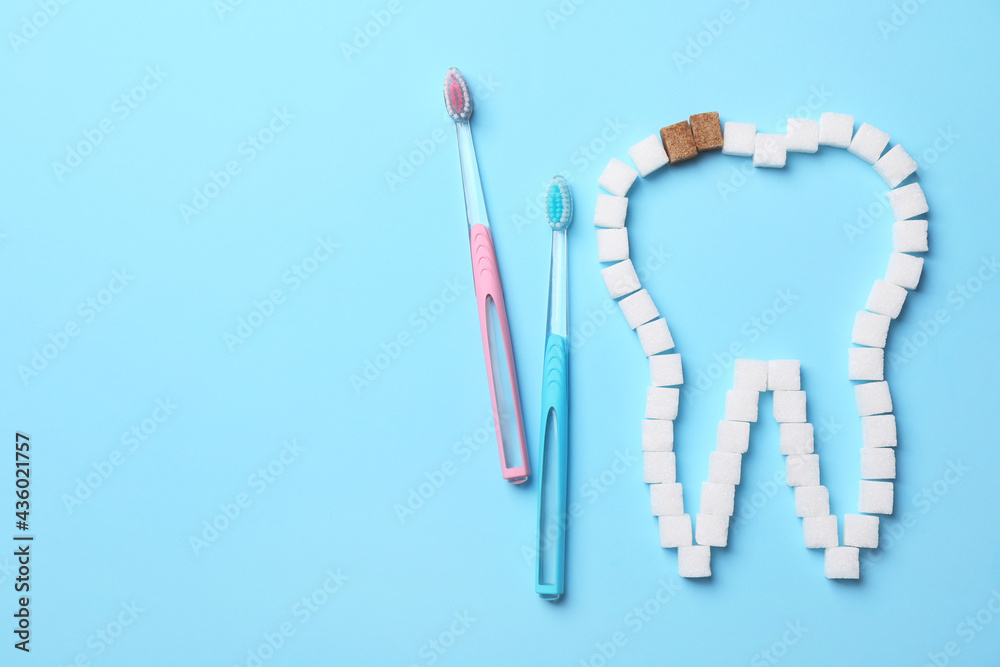 Composition with tooth outline made of sugar cubes near toothbrushes, flat lay. Caries problem Composition with tooth outline made of sugar cubes near toothbrushes, flat lay. Caries problem