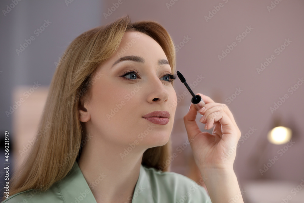 Reflection of beautiful young woman applying mascara in mirror at home Reflection of beautiful young woman applying mascara in mirror at home