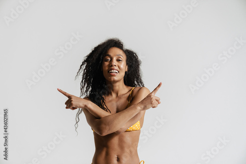Black woman in swimsuit smiling and pointing fingers at opposite sides