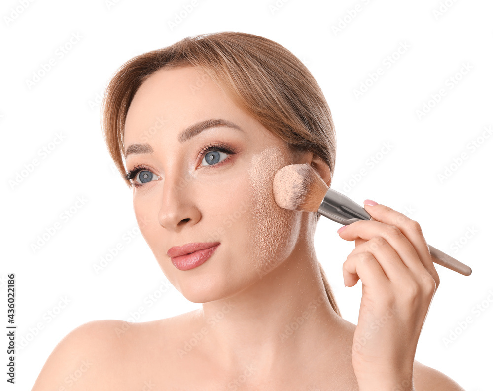 Beautiful young woman applying face powder with brush on white background