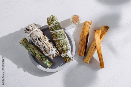 White sage, cedar, sweetgrass, and Palo Santo sticks tied by a bunch on a light background. Set of incense for fumigation, illuminated by the sun. Top view. Organic incense from Latin America.