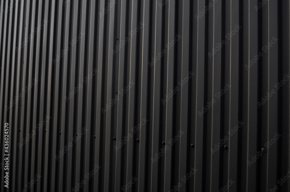 Obraz premium Black corrugated iron sheet used as a facade of a warehouse or factory. Texture of a seamless corrugated zinc sheet metal aluminum facade. Architecture. Metal texture.