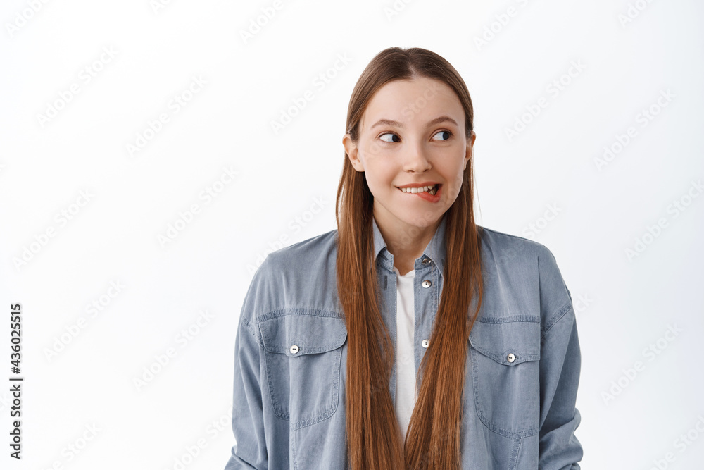 Excited pensive girl smiling, biting lip from desire and temptation, looking aside at copy space, your logo banner, standing dreamy against white background Excited pensive girl smiling, biting lip from desire and temptation, looking aside at copy space, your logo banner, standing dreamy against white background
