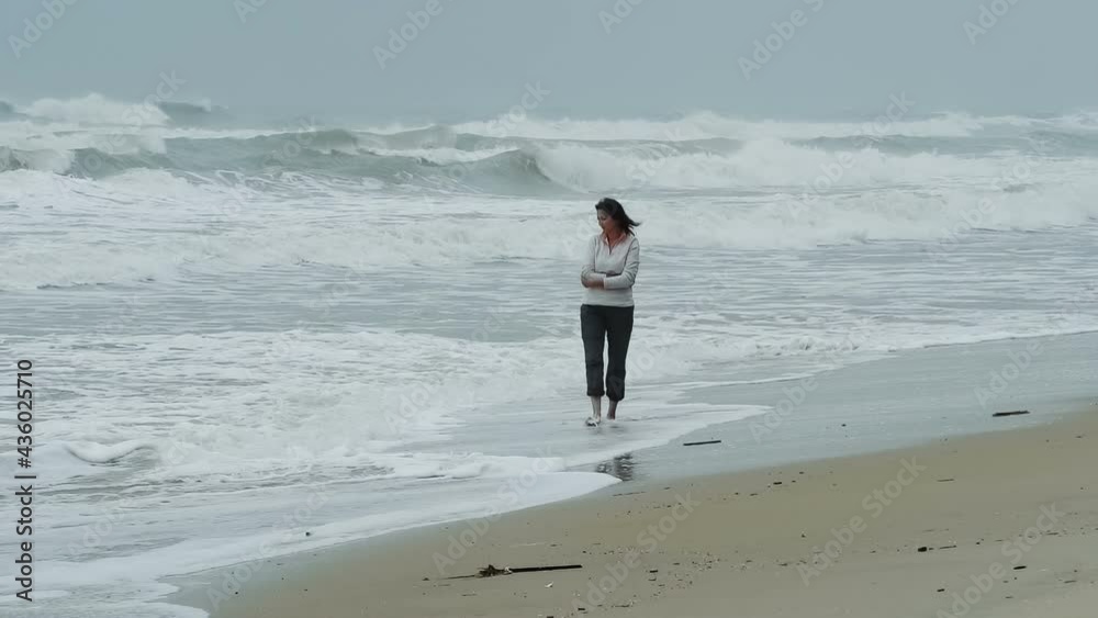 Attractive woman walking the beach with bad stormy weather - looking at the sea. Slow motion people footage. Attractive woman walking the beach with bad stormy weather - looking at the sea. Slow motion people footage.