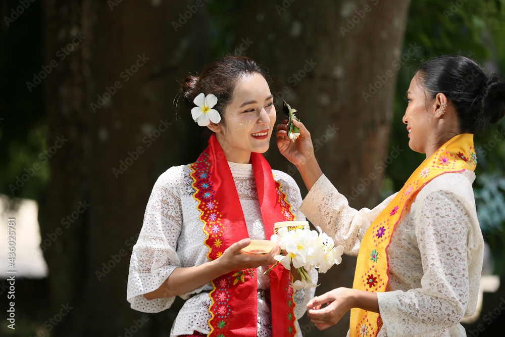 Two Myanmar women holding flowers at a temple. Southeast Asian young girls with burmese traditional dress visiting a Buddihist