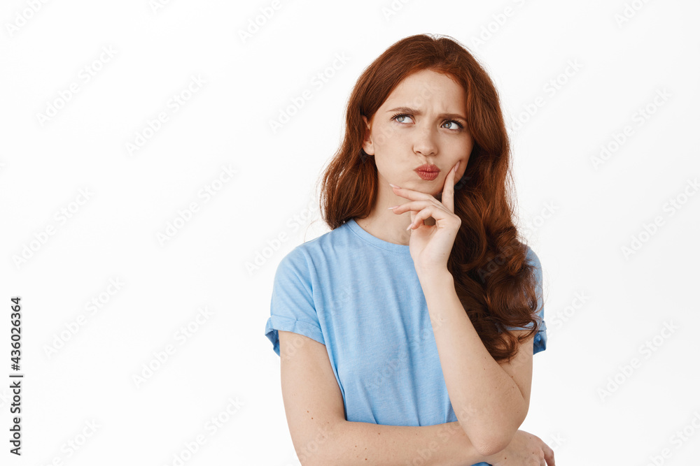 Image of thoughtful hesitant girl with red hair making decision, frowning perplexed and thinking, touching lip pondering, standing against white background Image of thoughtful hesitant girl with red hair making decision, frowning perplexed and thinking, touching lip pondering, standing against white background