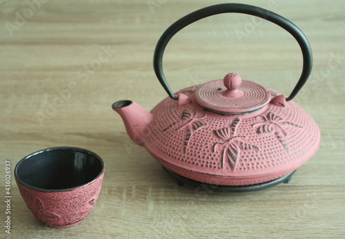 A Japanese-style cast-iron teapot with a matching cup on a wood-effect tabletop. Natural lighting from the right.