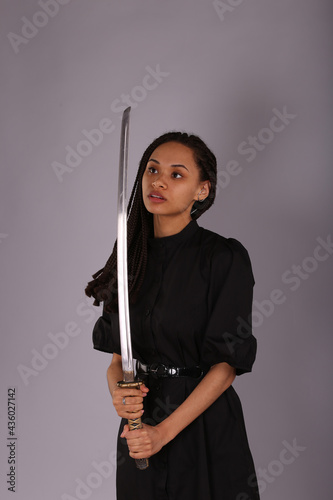 Beautiful woman in black dress with katana sword on grey background