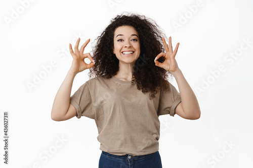 Portrait of proud and happy girl praising you, showing okay Ok gesture and smiling satisfied, support friend, encourage someone, approve and like something, standing over white background