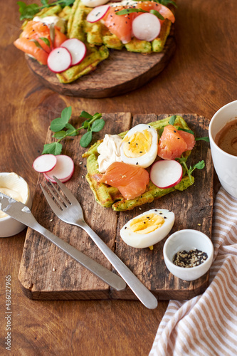 Spinach waffles with salmon, egg and radish. Side view, wooden background.