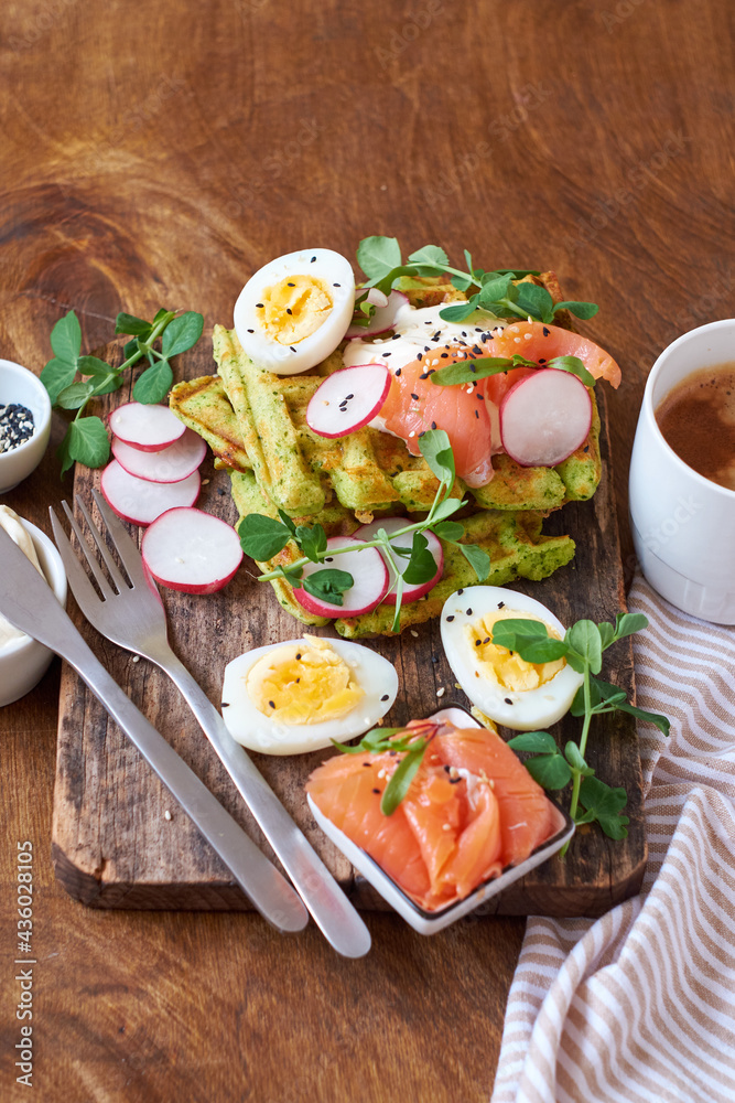 Spinach waffles with salmon, egg and radish. Side view, wooden background.