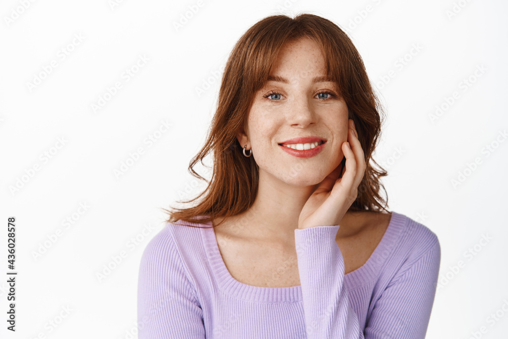 Beauty. Tender and feminine girl touching her healthy, natural skin, showing cosmetology after effect, smiling happy, standing in purple blouse against white background Beauty. Tender and feminine girl touching her healthy, natural skin, showing cosmetology after effect, smiling happy, standing in purple blouse against white background