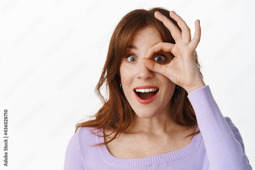 Close up portrait of excited stylish girl, looking through OK okay sign against eye, watching something awesome, recommending good thing, praise product or company, standing over white background Close up portrait of excited stylish girl, looking through OK okay sign against eye, watching something awesome, recommending good thing, praise product or company, standing over white background
