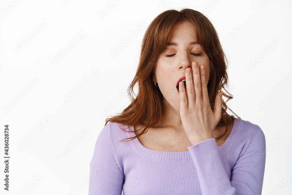 Close up of tired young stylish girl, yawning sleepy after partying all night, covering opened mouth and yawn, standing bored against white background Close up of tired young stylish girl, yawning sleepy after partying all night, covering opened mouth and yawn, standing bored against white background