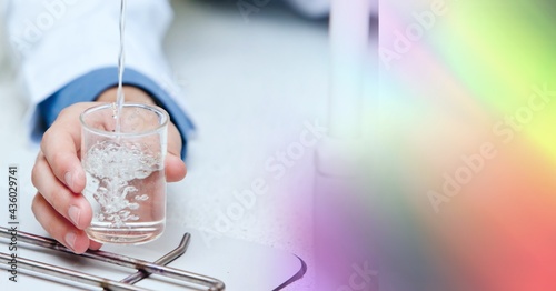 Composition of hand holding liquid in chemistry beaker, with blurred colourful copy space to right