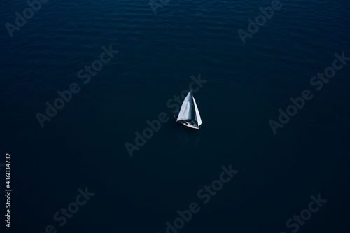 Sailboat on Lake Garda, Italy. Boat with sails, blue water with high altitude. Large white boat with sails on blue water aerial view. Lonely sailboat on the water top view.